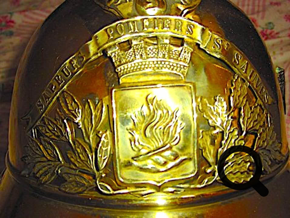 Casque en métal doré avec un écusson représentant des flammes et des branches, entouré des mots "Sapeurs Pompiers".