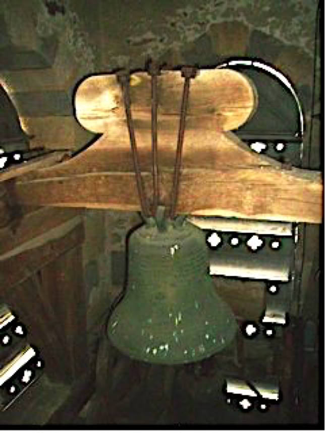 Cloche en métal suspendue à une structure en bois à l'intérieur d'un bâtiment en pierre avec des fenêtres en arrière-plan.