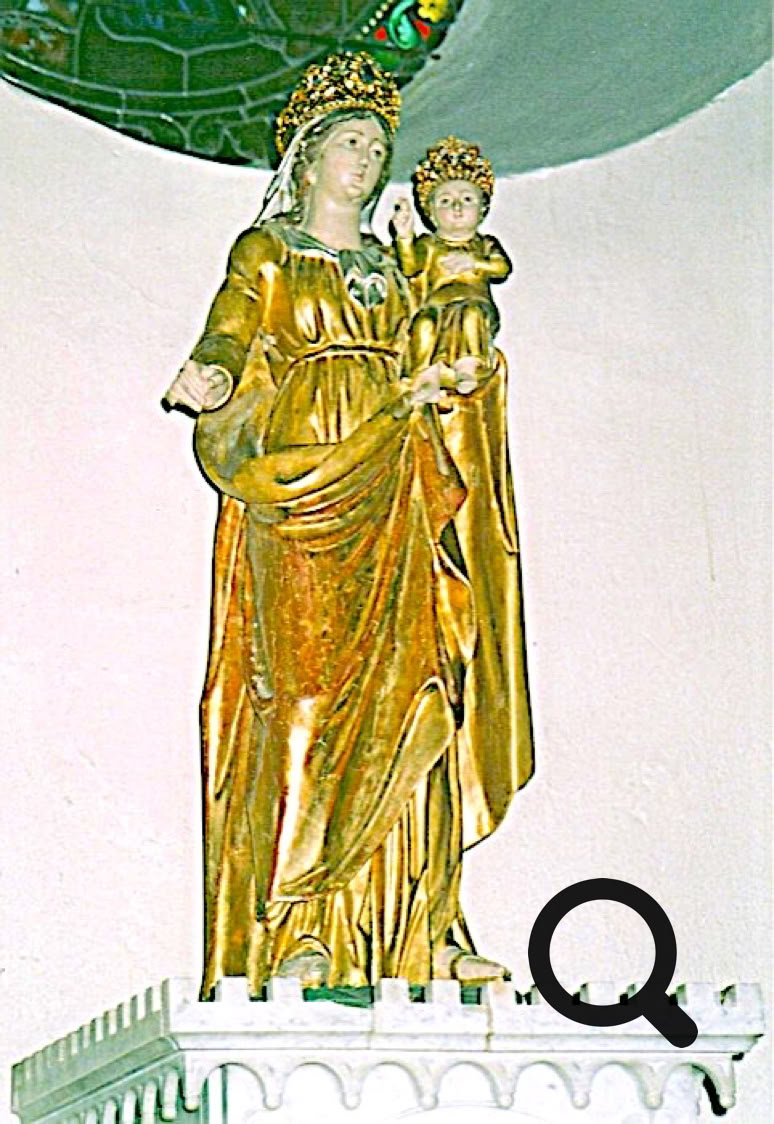 Statue dorée d'une femme couronnée tenant un enfant, posée sur un socle blanc avec un vitrail en arrière-plan.