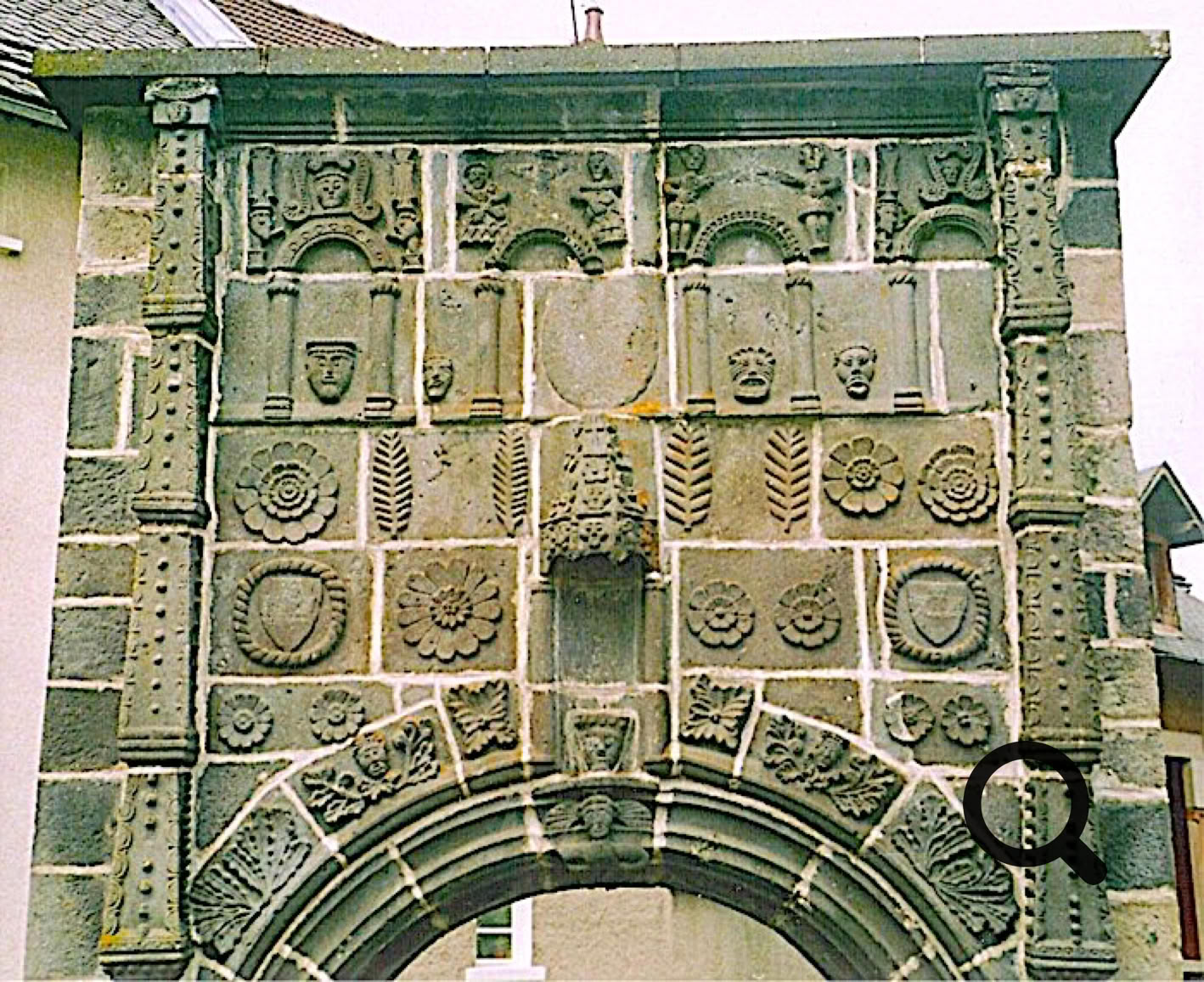 Arc en pierre décoré de motifs sculptés et de blasons, avec des détails architecturaux complexes.