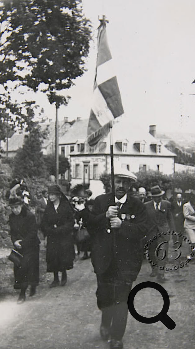 Groupe de personnes marchant dans une rue, l'une d'elles portant un drapeau. Un bâtiment est visible en arrière-plan.