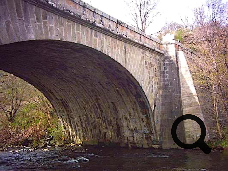 Pont en arc en pierre au-dessus d'une rivière, entouré d'arbres.