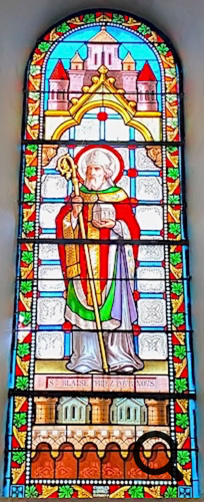 Vitrail représentant une figure religieuse en robe avec une crosse, entourée d'éléments architecturaux et de motifs colorés.