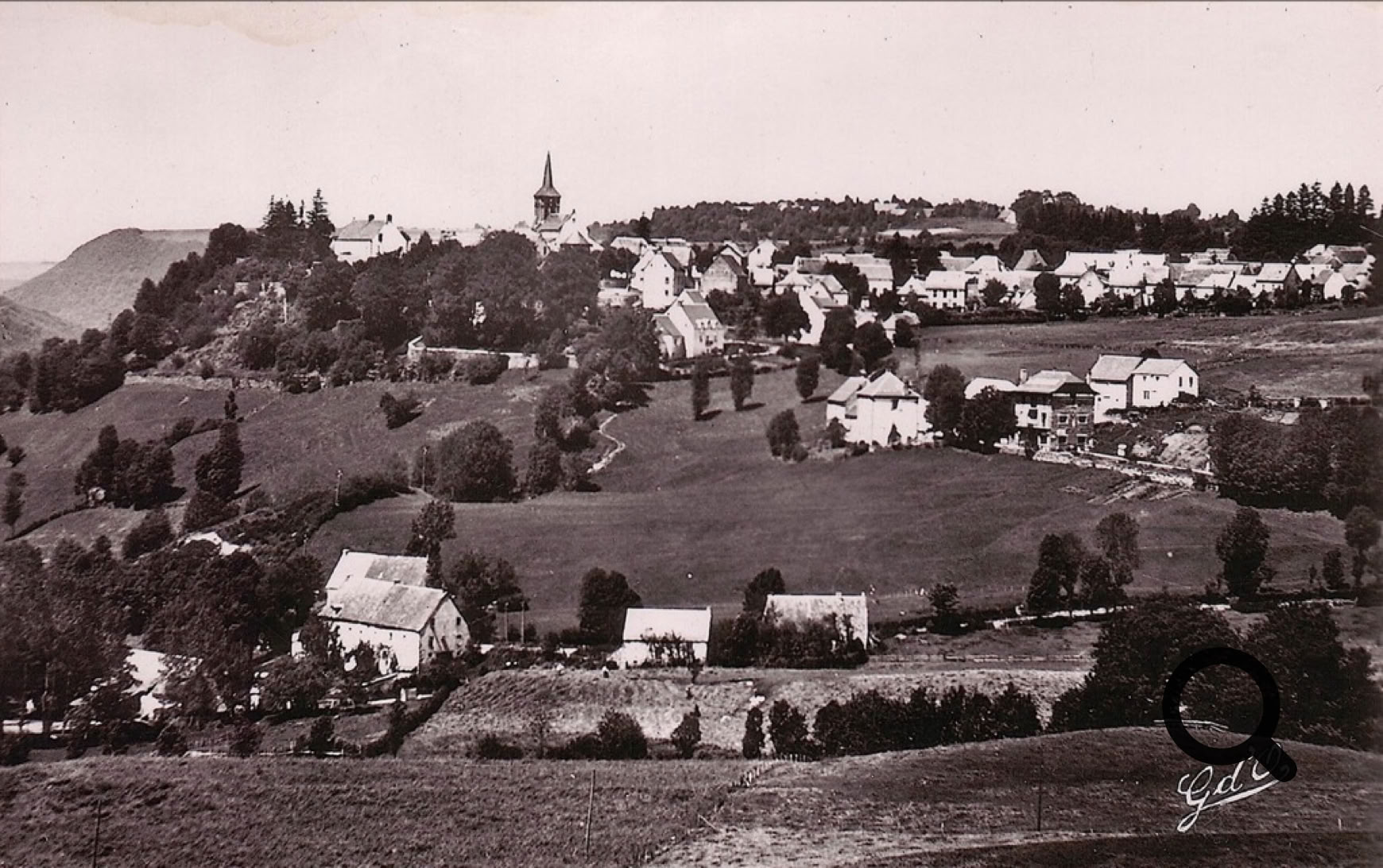 Vue d'un village rural avec des maisons dispersées, des champs et une église sur une colline.