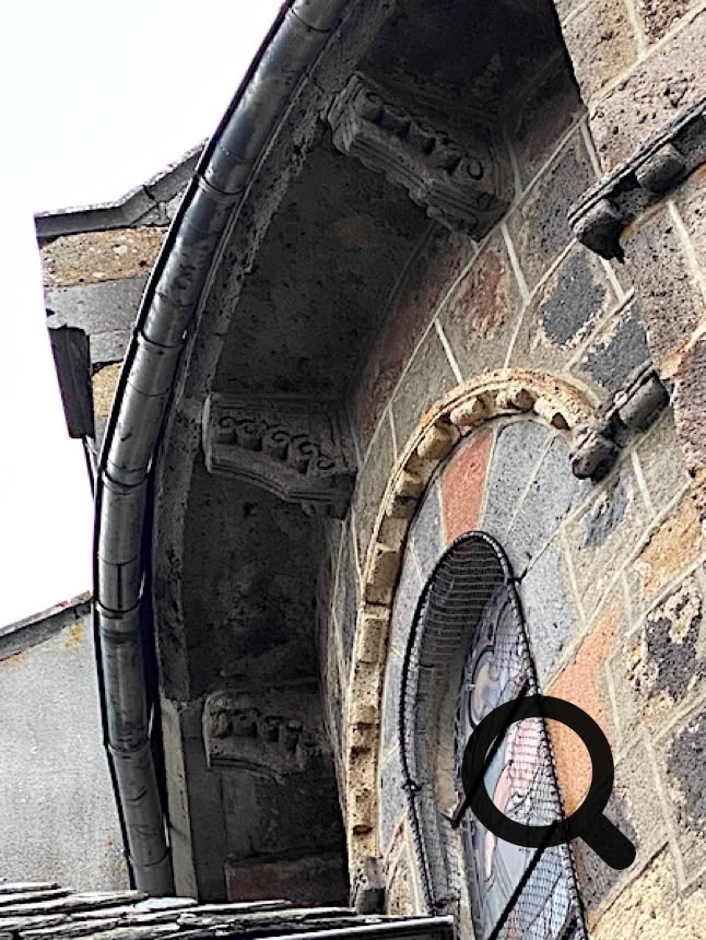 Mur en pierre avec une fenêtre en arc et des détails architecturaux sous le toit.