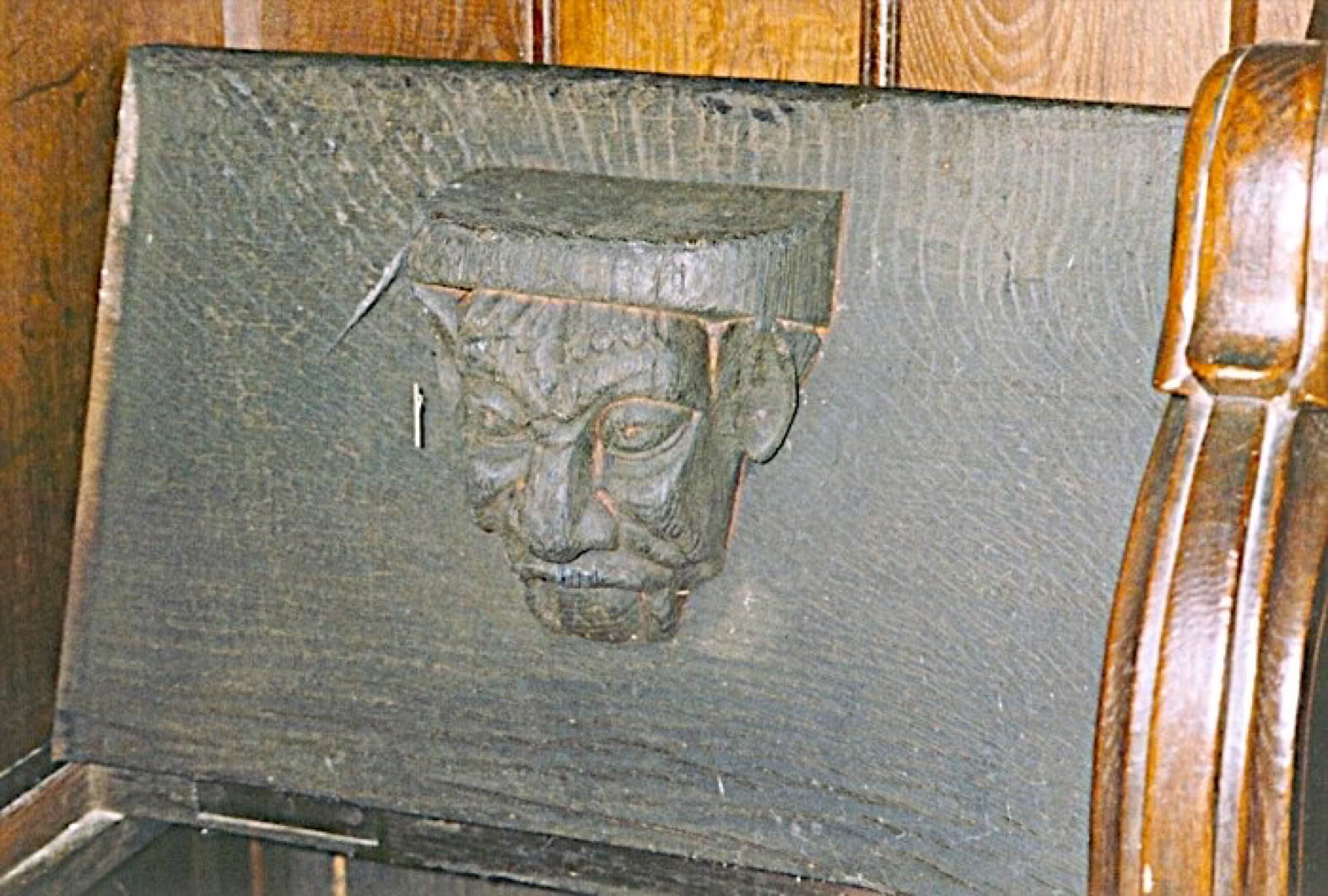 Bas-relief en bois représentant un visage sculpté sur le dossier d'un banc en bois.