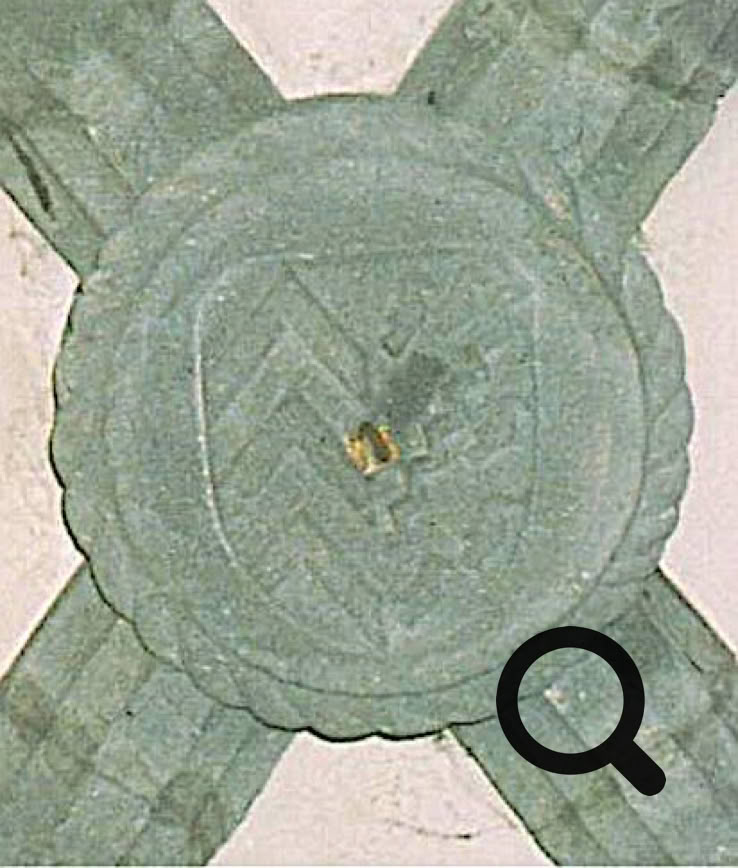 Sculpture circulaire en pierre avec un blason au centre, entourée de motifs en forme de croix.