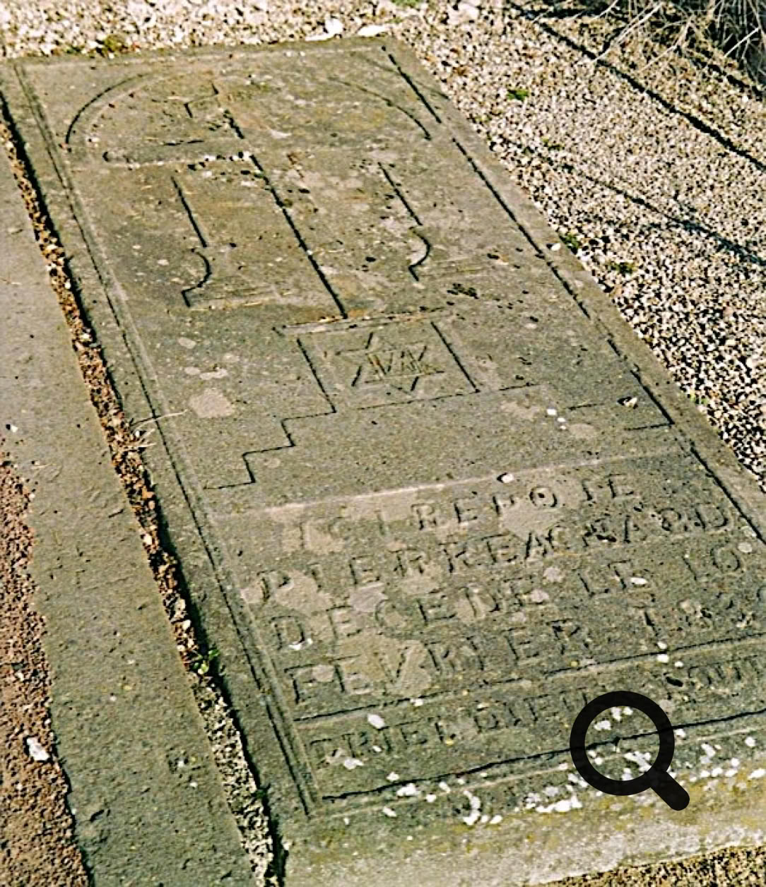 Pierre tombale ancienne avec des inscriptions gravées, entourée de gravier.