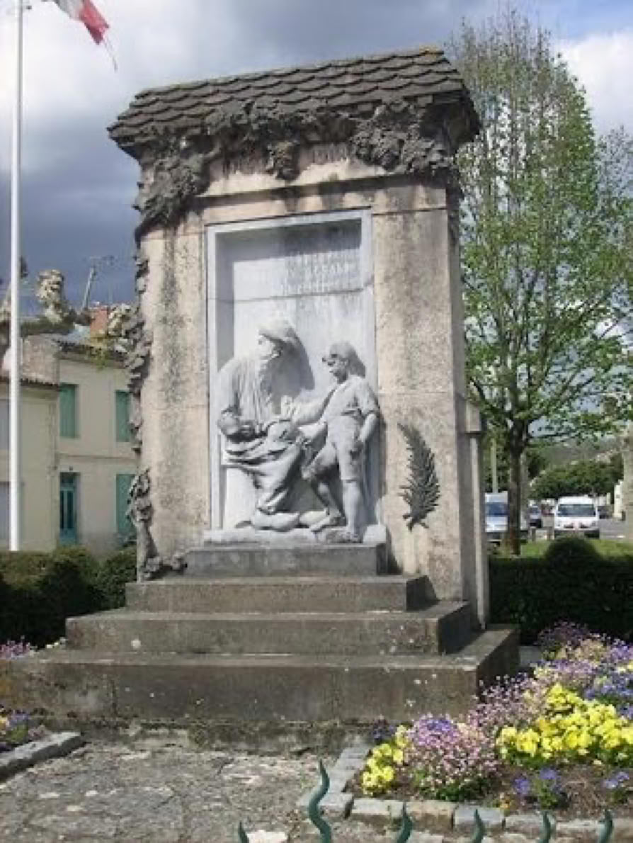 Monument en pierre avec une sculpture représentant deux figures, entouré de fleurs et de végétation, avec un ciel nuageux en arrière-plan.