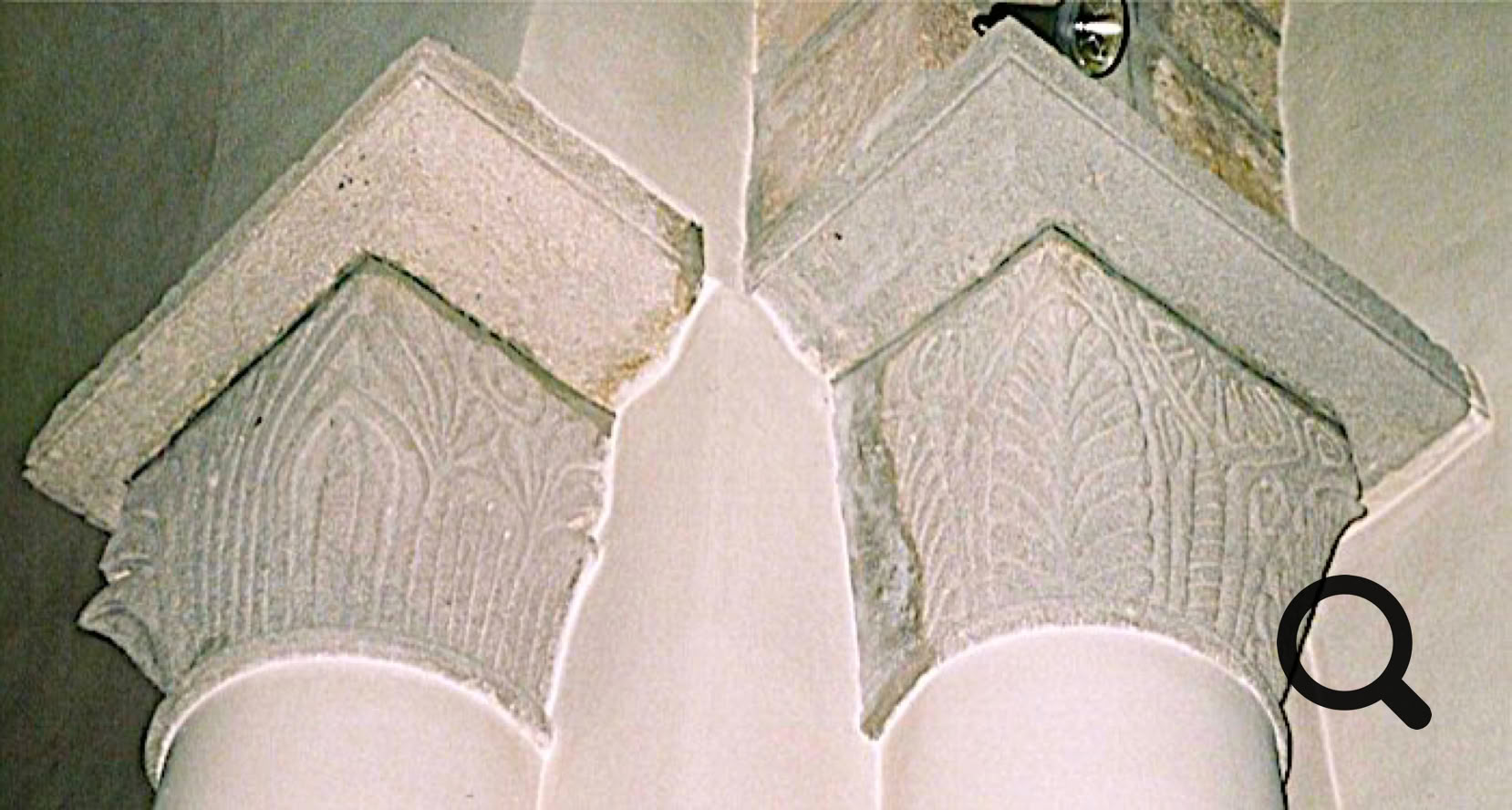 Deux chapiteaux sculptés en pierre avec des motifs géométriques, surmontant des colonnes blanches.