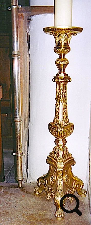 Chandelier en métal doré avec une bougie blanche sur le dessus, posé sur un sol en pierre.