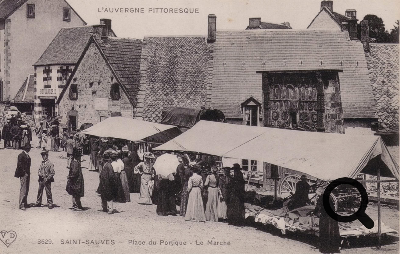 Scène de marché en plein air avec des étals et des personnes devant des maisons anciennes.