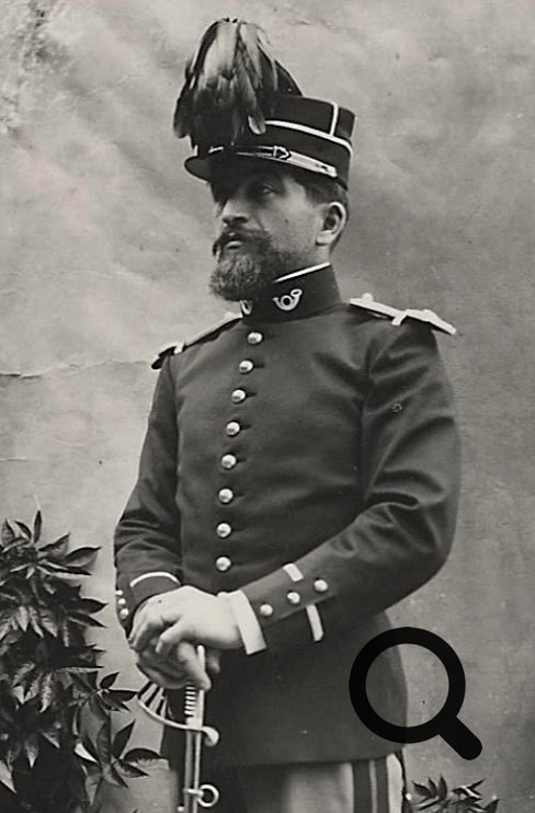 Marius Vazeilles en uniforme avec un chapeau à plume, tenant un sabre, debout devant un mur avec des plantes à gauche.