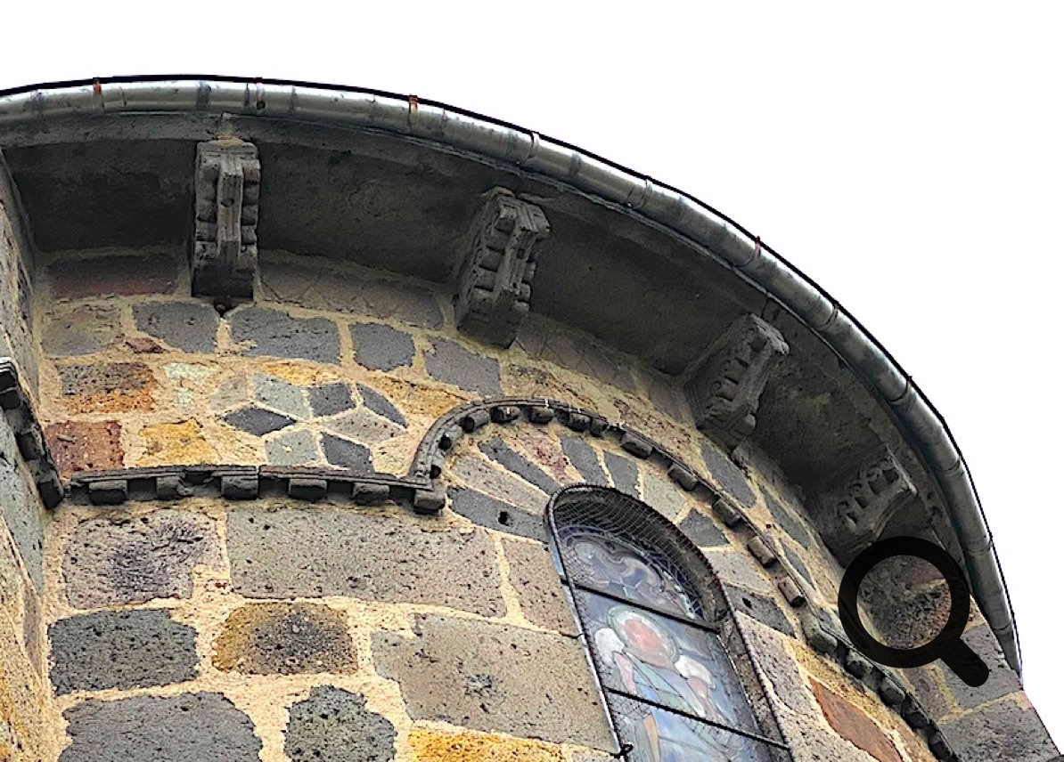 Mur en pierre du bâtiment avec une fenêtre en arc et des détails architecturaux sous le toit.