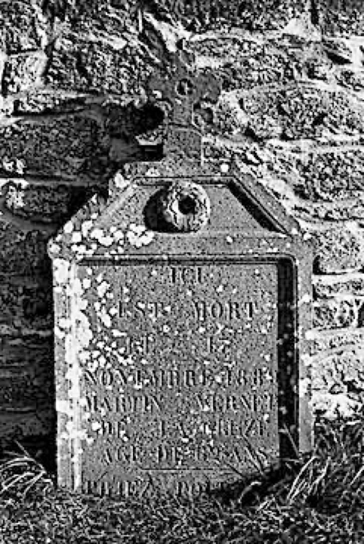 Vieille pierre tombale avec des inscriptions usées, adossée à un mur de pierre.