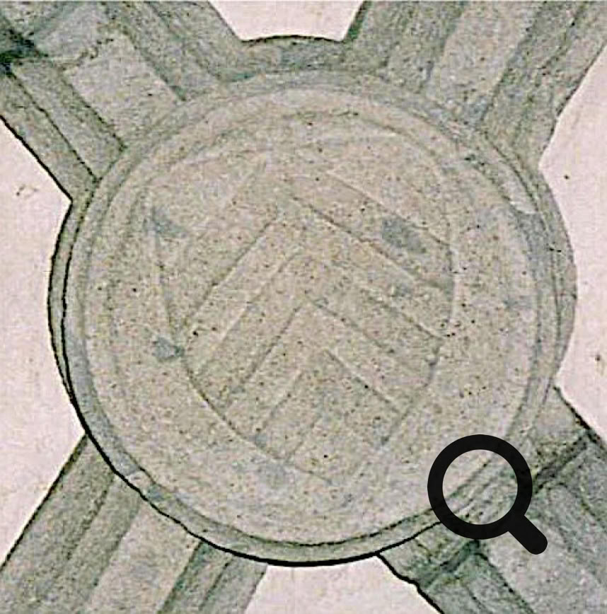 Pierre sculptée avec un motif de chevrons dans un cercle, entourée de lignes croisées.