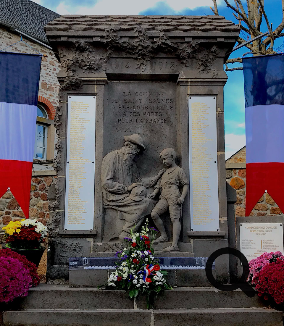 Monument en pierre avec deux figures sculptées, entouré de fleurs et de drapeaux tricolores.