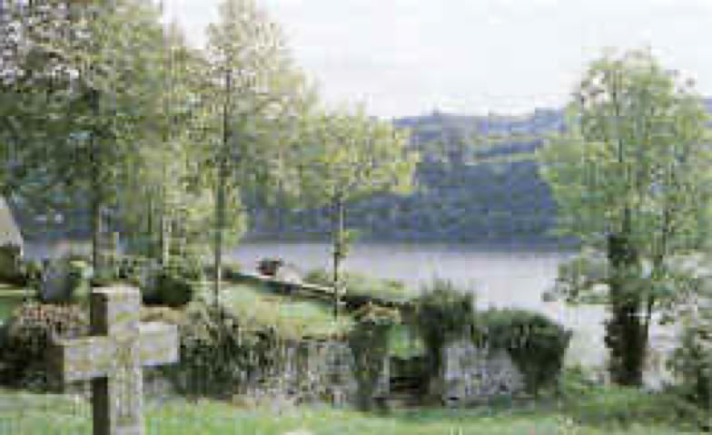 Paysage avec des arbres, une croix en pierre et un lac en arrière-plan.