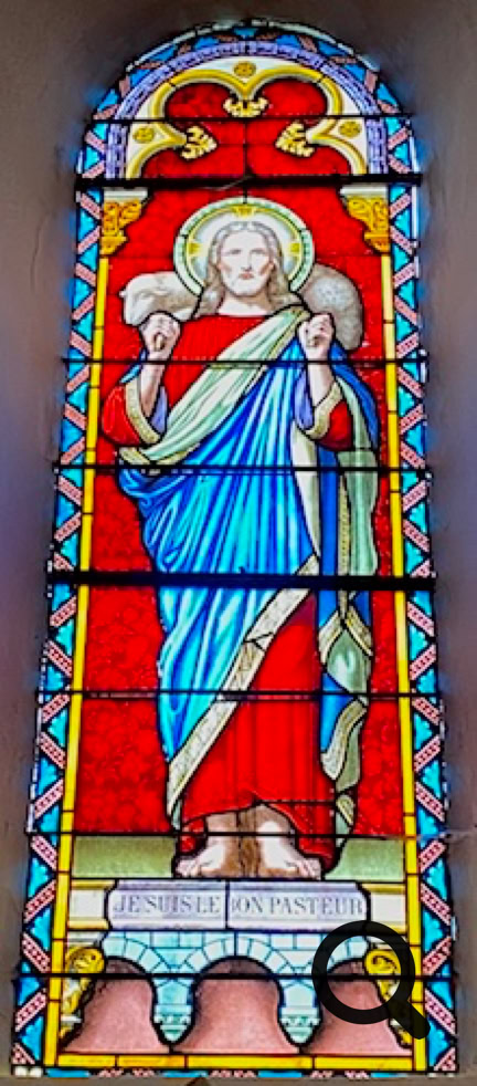 Vitrail représentant une figure religieuse avec une auréole, vêtue de bleu et de rouge, sur un fond rouge.